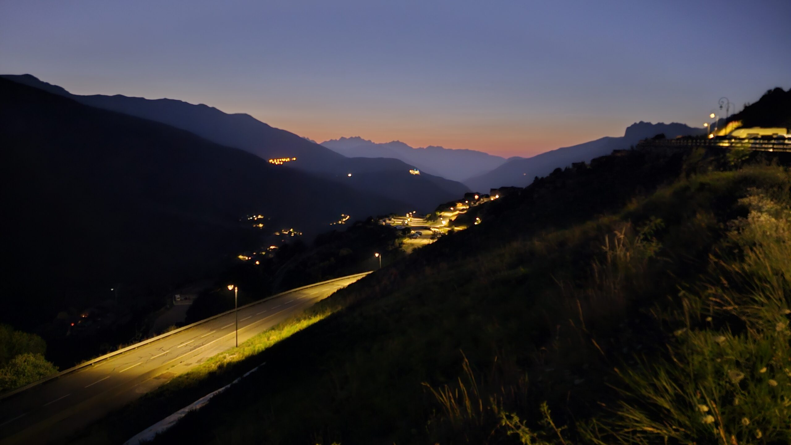 Vue nocturne depuis les hauteurs de Valmeinier, avec la route illuminée serpentant dans la vallée des Alpes