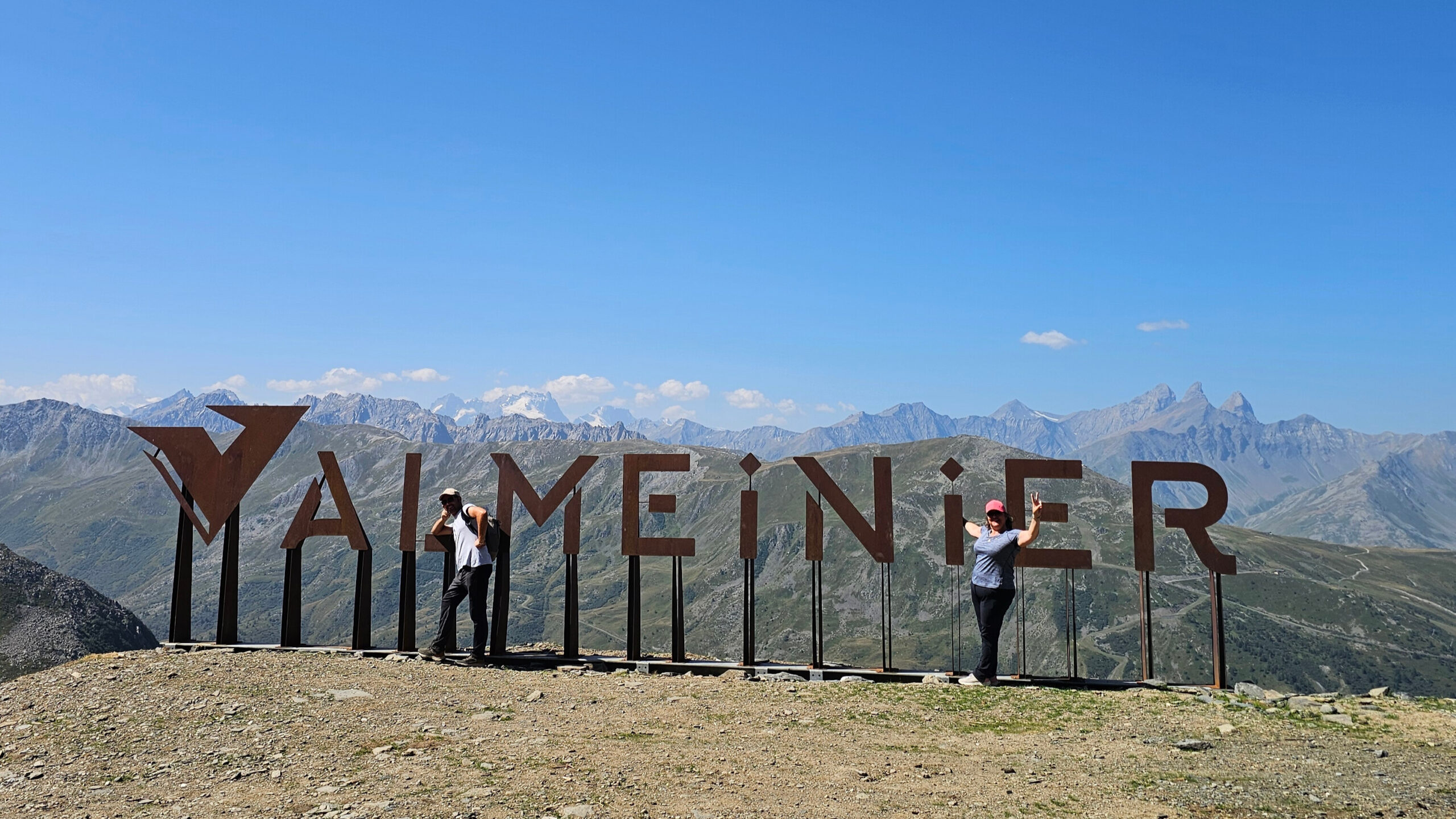 Vue panoramique depuis le télésiège des Jeux à Valmeinier, avec les lettres en tôle rouillée et le massif des Écrins en arrière-plan