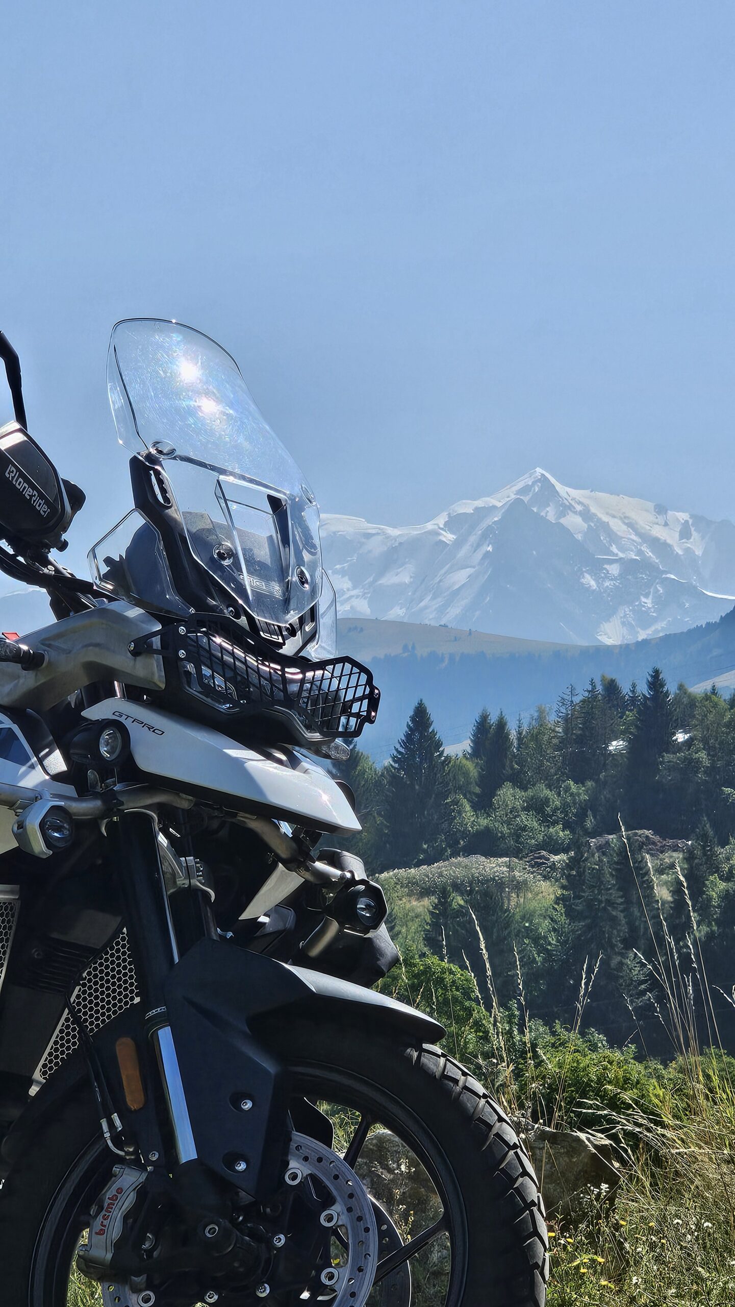 Avant d’une moto Triumph Tiger avec le Mont-Blanc en toile de fond, sur une route alpine