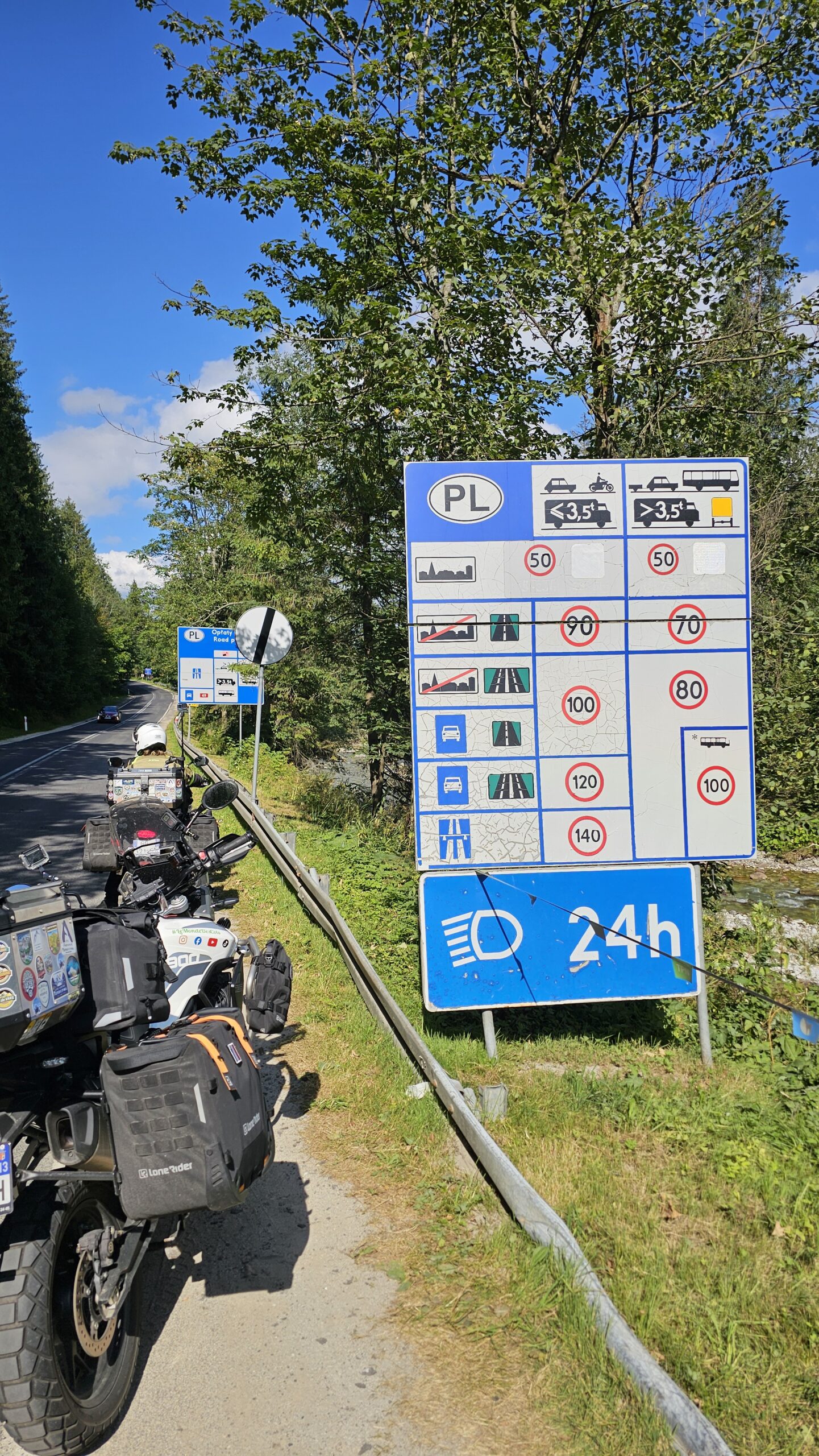 Photo de nos deux motos Triumph Tiger garées sous le panneau d’entrée “Polska”, marquant notre arrivée en Pologne.