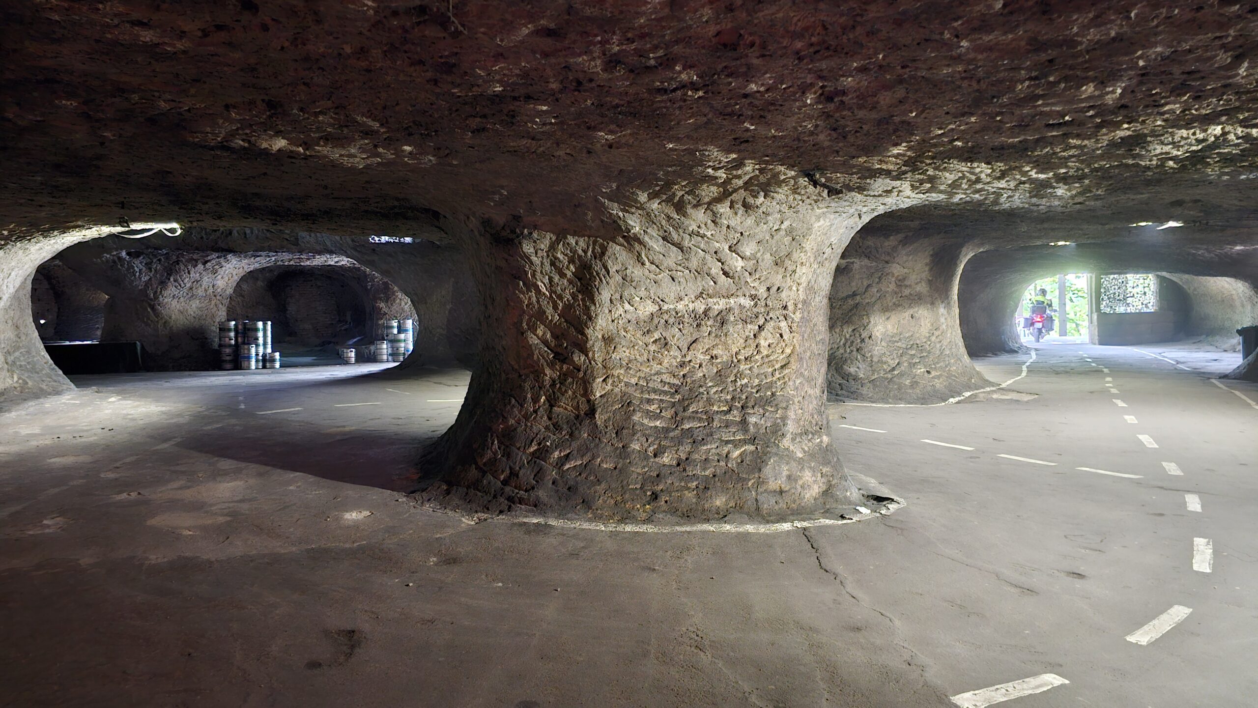 Photo intérieure des Grottes de l’Enfer en République tchèque, avec cavités rocheuses sombres et sol goudronné éclairé par la lumière.