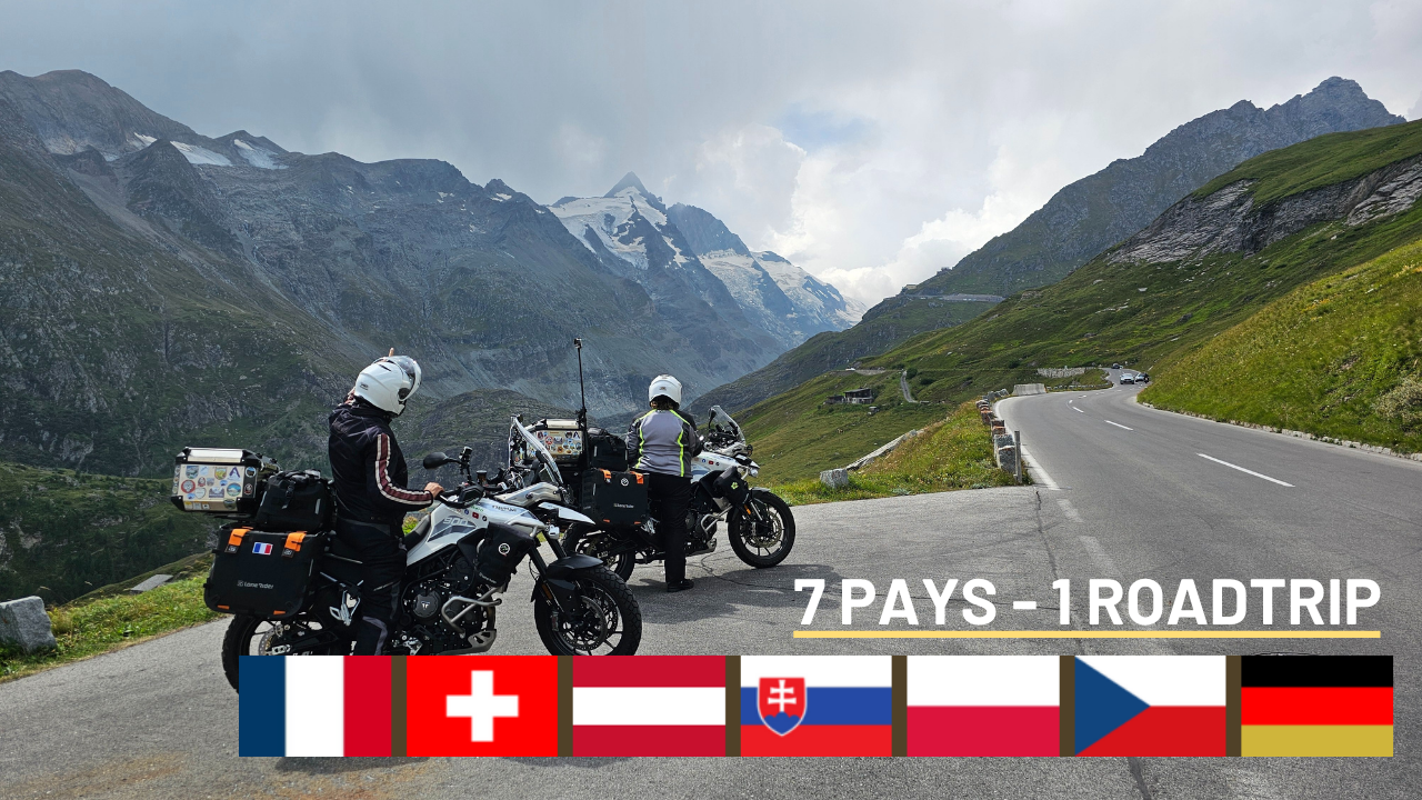 Deux motards de dos contemplent le sommet du Grossglockner en Autriche, la route à leurs côtés et les drapeaux des sept pays traversés : France, Italie, Autriche, Slovaquie, Pologne, République tchèque et Allemagne.