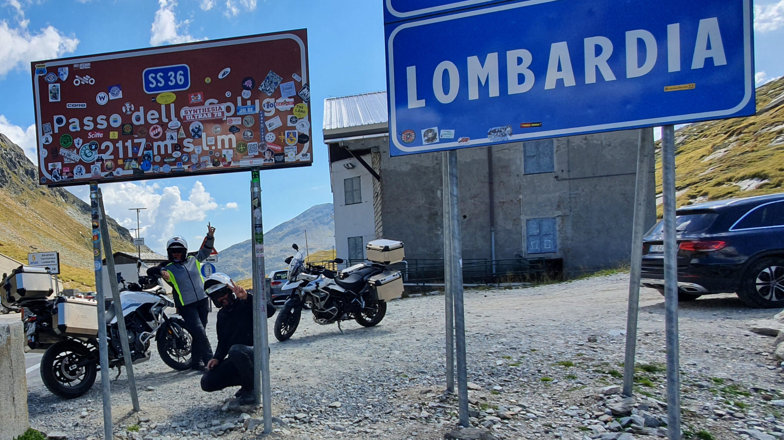 Deux motos Triumph Tiger 900 GT Pro devant le panneau du sommet du Passo dello Spluga.