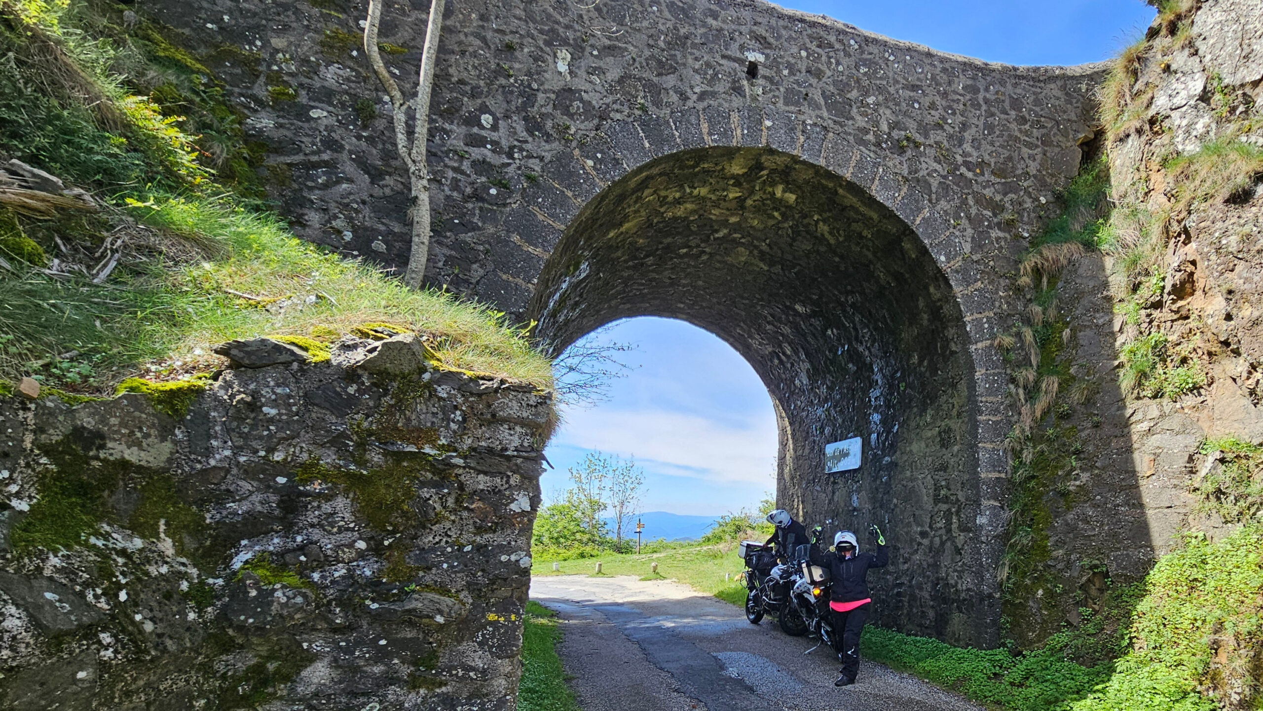 Entrée du tunnel du col de l'Asclier à moto côté nord avec le panneau de col suspendu sous la voûte en pierre.