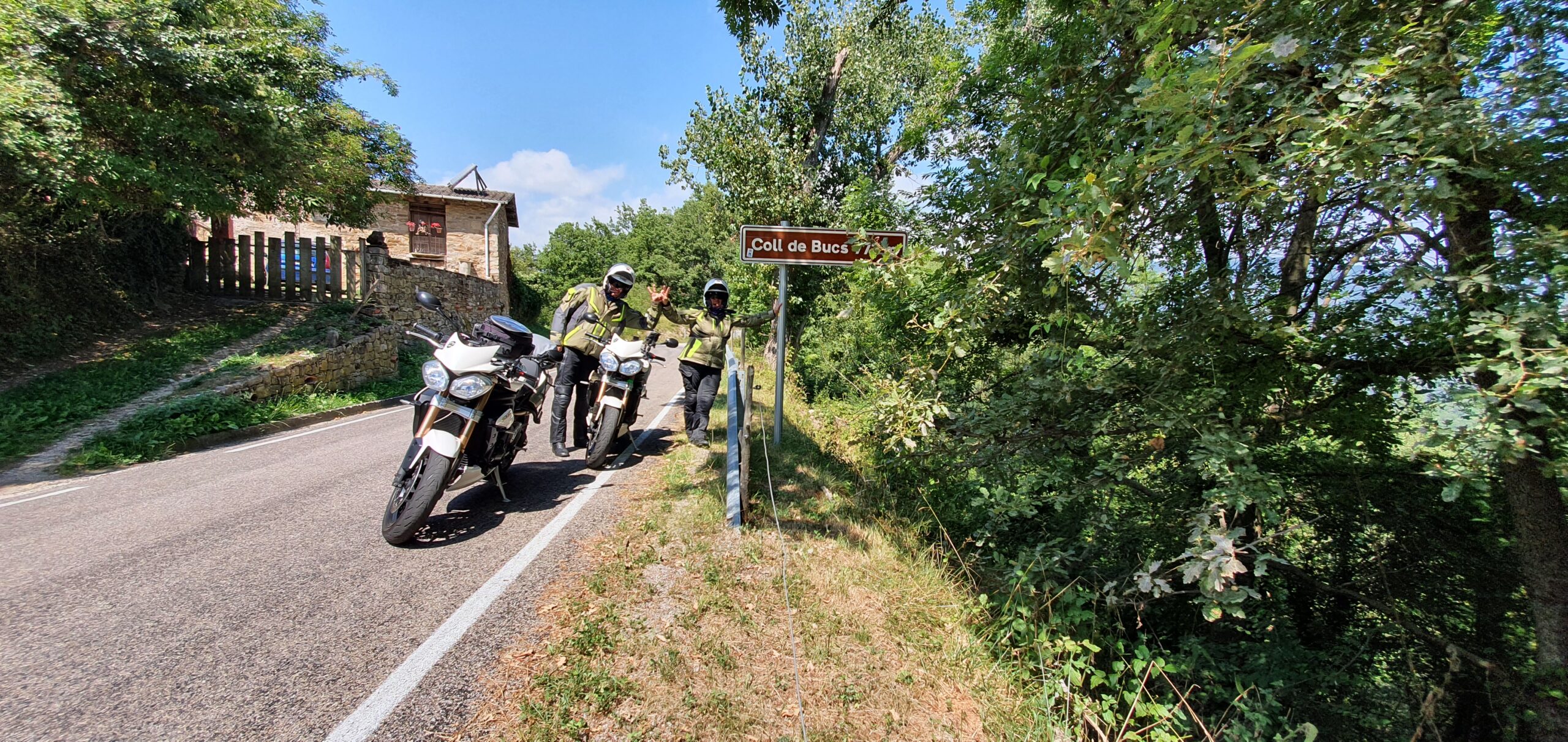 Deux Triumph Speed Triple 1050 garées au sommet du Coll de Bucs avec les motards faisant le signe V.