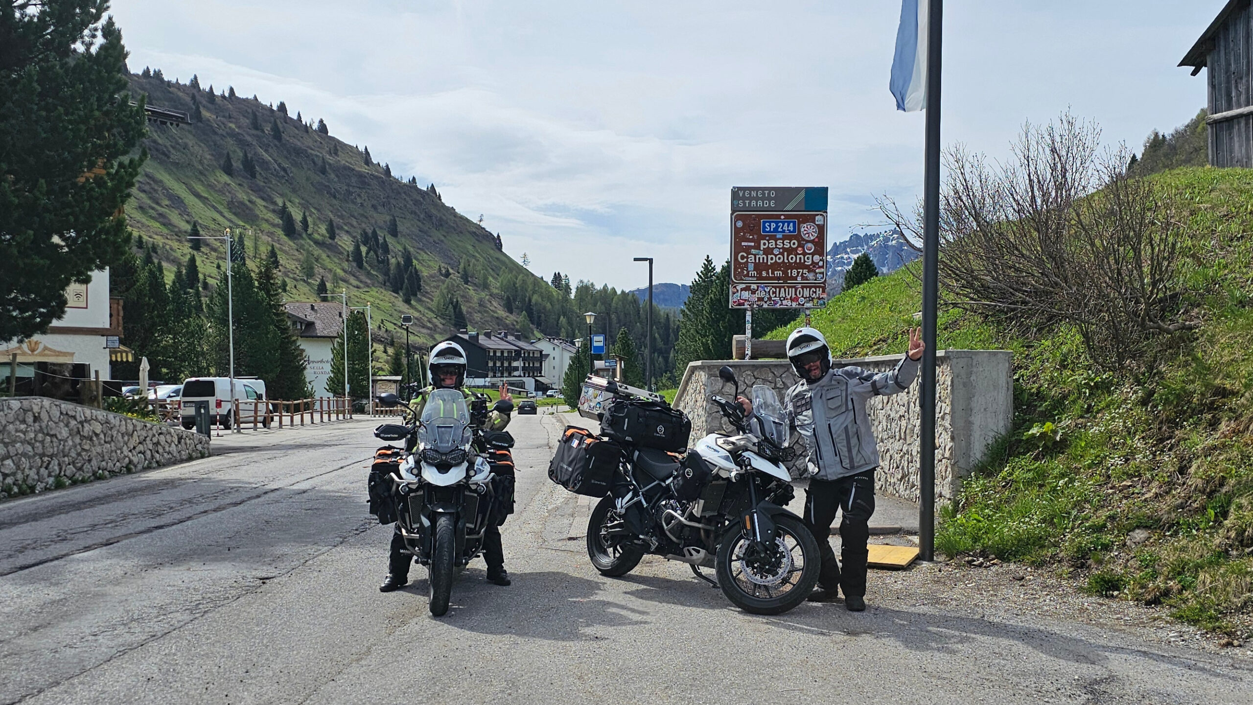 Cristian debout faisant le signe V du motard devant sa moto équipée Lone Rider au Passo Campolongo.