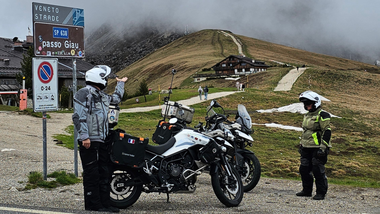Triumph Tiger 900 GT Pro devant le panneau du Passo Giau sous un ciel couvert dans les Dolomites