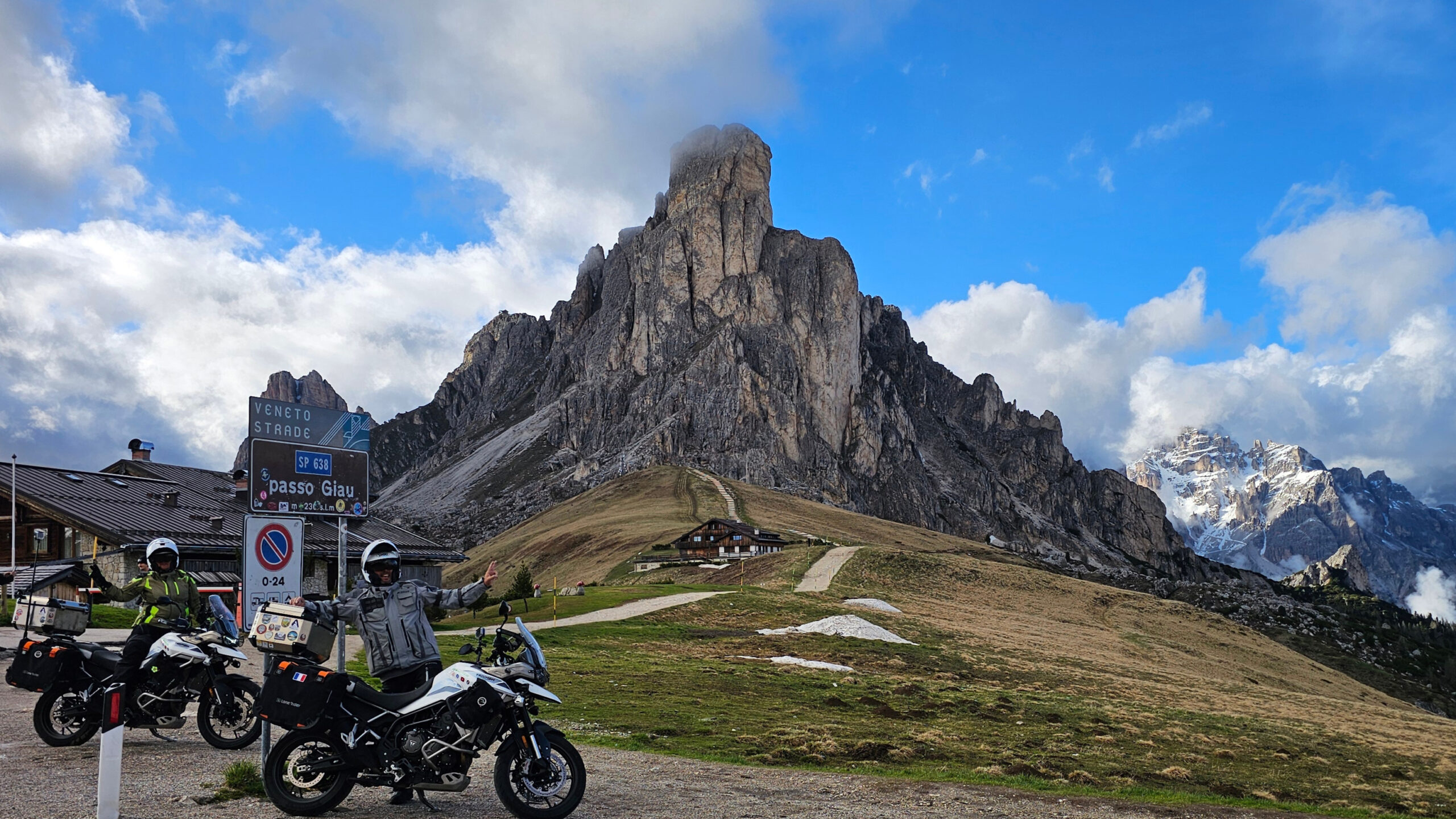 Triumph Tiger 900 GT Pro devant le panneau du Passo Giau par beau temps dans les Dolomites