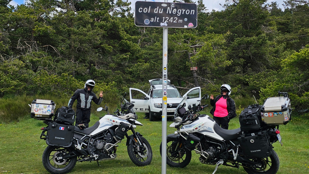 Signe du motard au sommet du col du Négron devant les Triumph Tiger équipées de bagagerie Lone Rider.