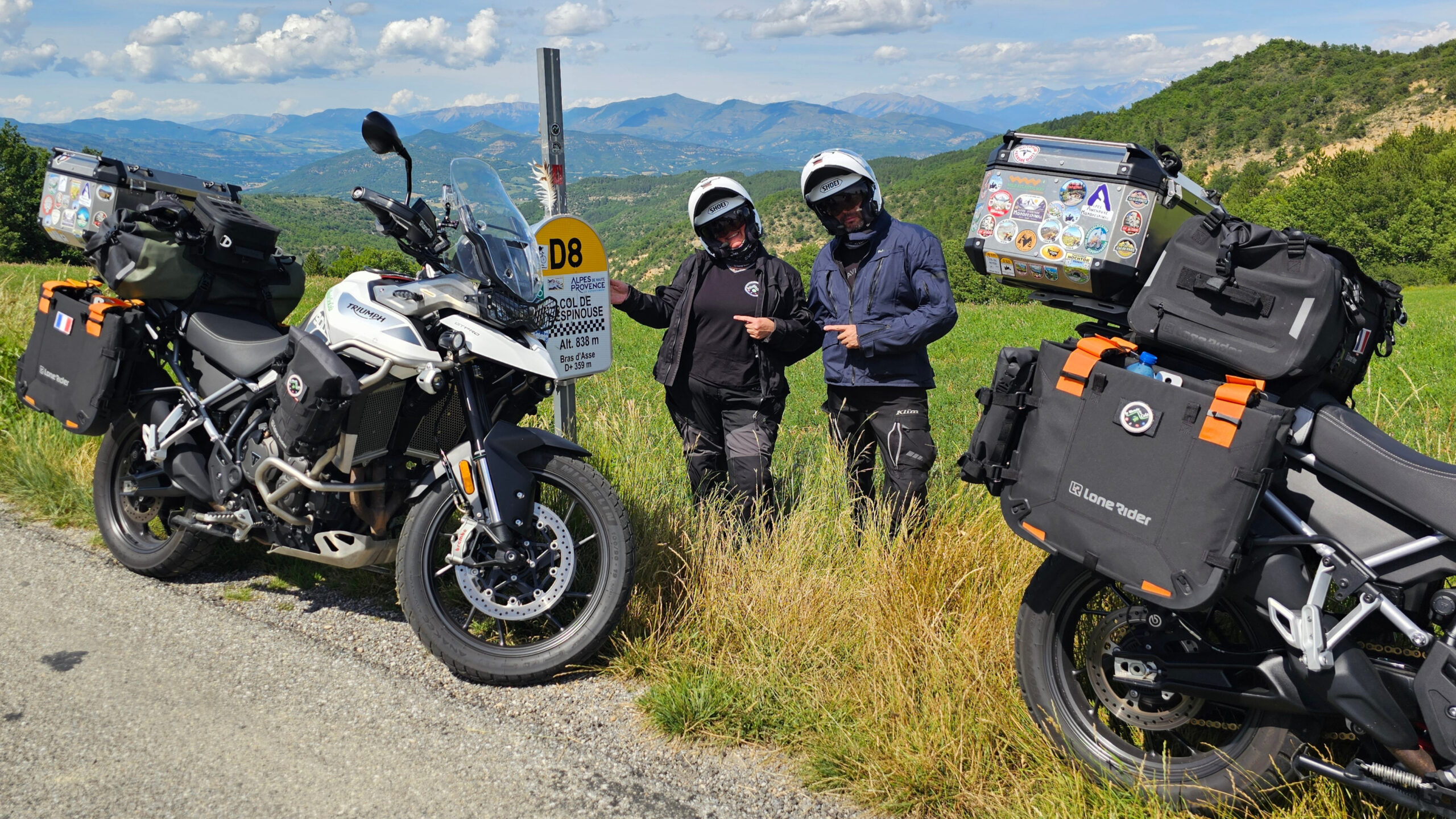 Motards debout à côté du panneau à damier du Col de l'Espinouse avec leurs motos équipées de bagagerie Lone Rider face au panorama.