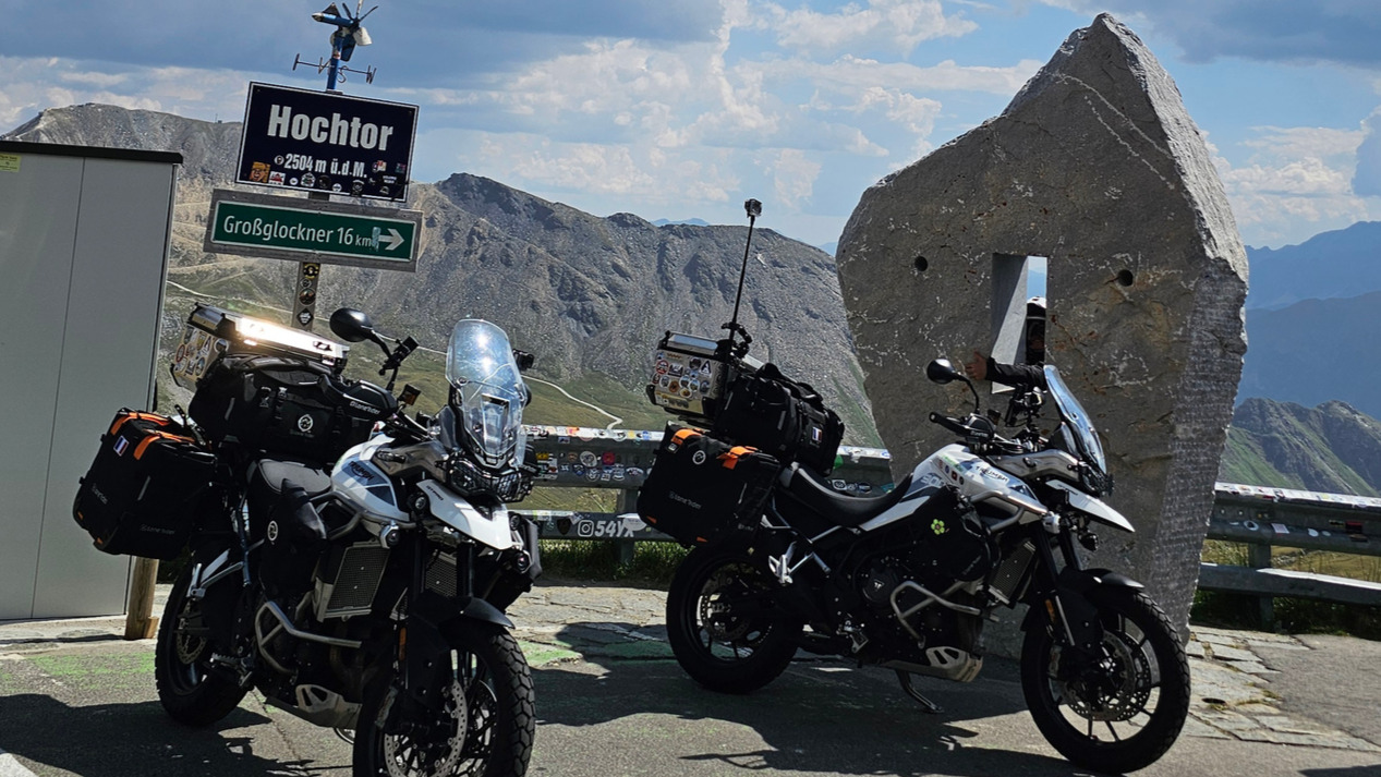 Deux motos Triumph Tiger avec bagagerie Lone Rider garées devant le panneau d'altitude du col de Hochtor.