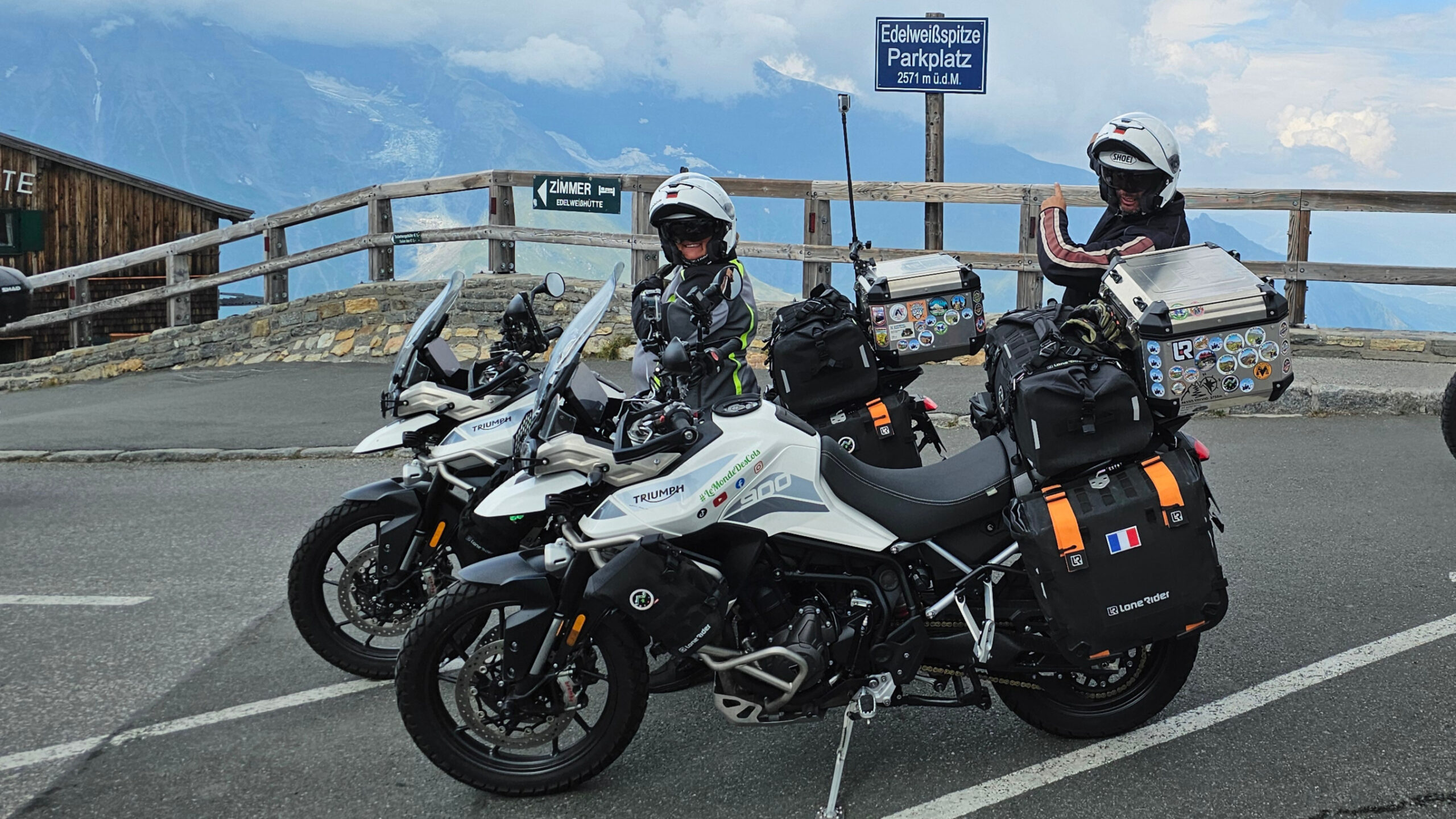 Motard et sa machine positionnés devant le panneau indicateur au sommet de l'Edelweissspitze