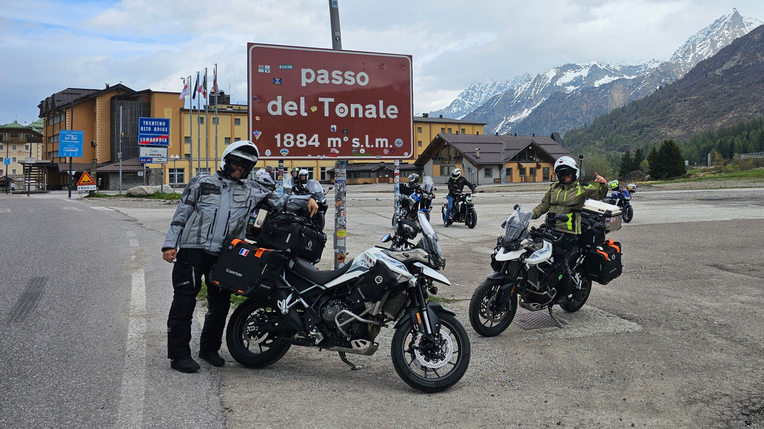 Motards avec sacoches LoneRider posant devant le panneau du Passo del Tonale et son large parking